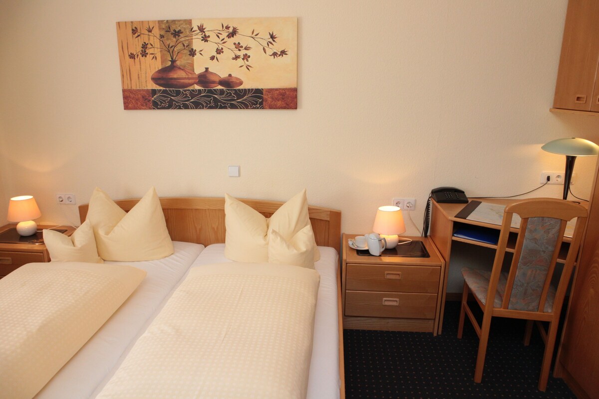 Une chambre d’hôtel comprenant un lit, deux tables de chevet, un bureau, une chaise et un tableau accroché au mur.