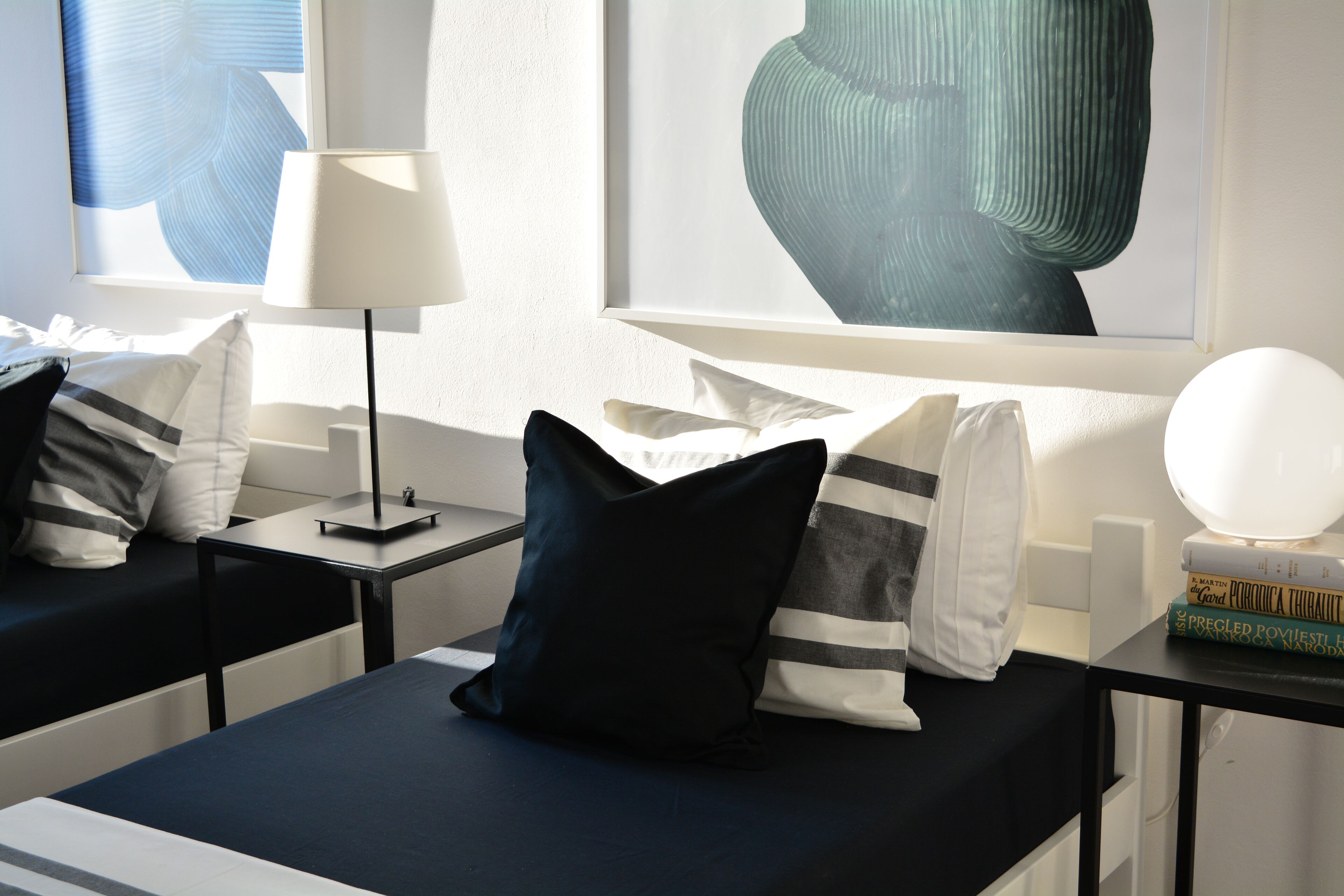 A modern hotel room with a bed, bedside tables, and a lamp. There are pillows and a book on the bedside table.