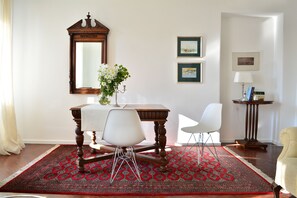 Un comedor con una mesa de madera, sillas blancas, un tapete rojo estampado, un espejo y cuadros en la pared.
