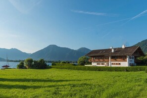 A traditional chalet-style building with a balcony, situated in a lush green field with a lake and mountains in the background. - Vacation apartment 2 - Seerose am See - Dream vacation directly on Lake Tegernsee (Bad Wiessee)