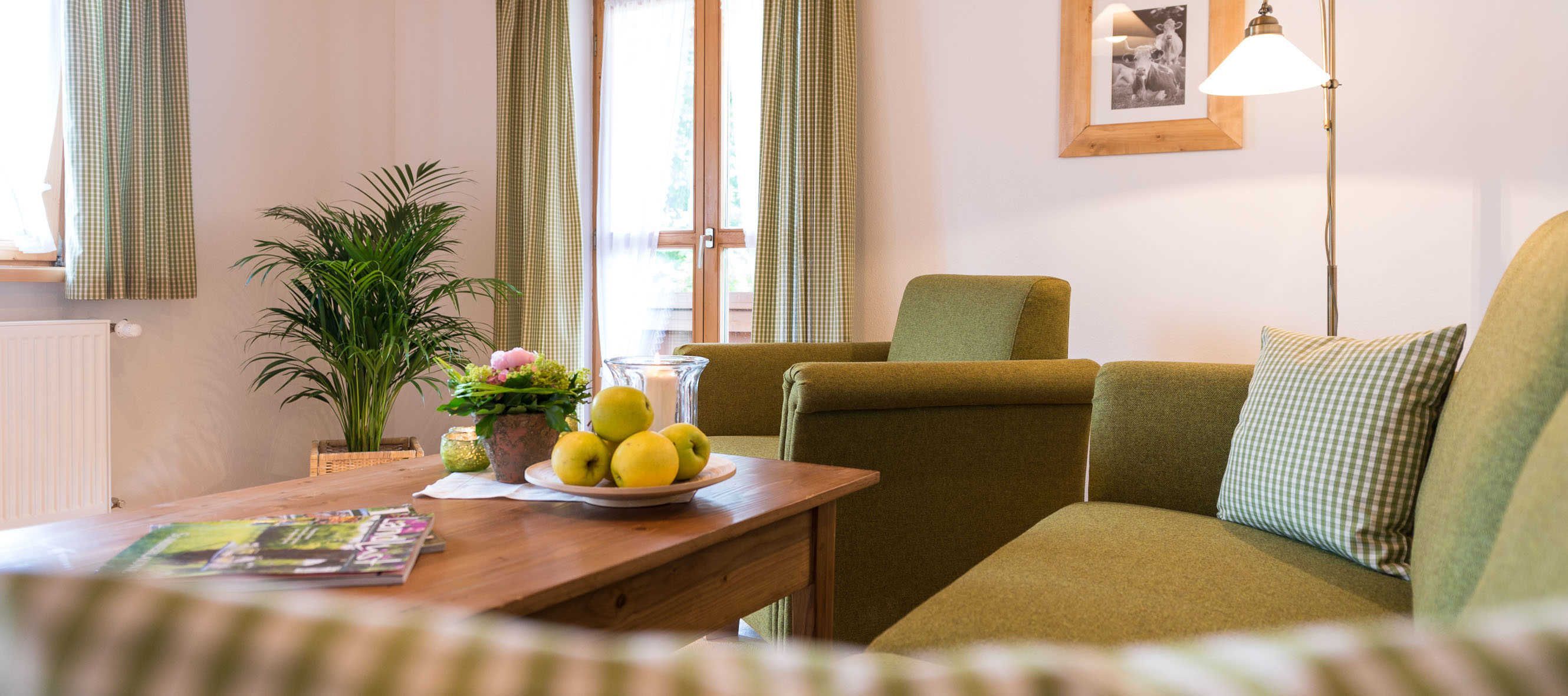 A cozy living room with a sofa, a table with a bowl of fruit, a potted plant, and a lamp.