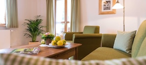 A cozy living room with a sofa, a table with a bowl of fruit, a potted plant, and a lamp.