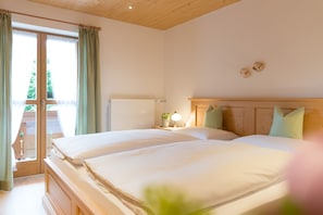 A double bed with a wooden headboard, a bedside table with a lamp, and a view through a glass door. - Vacation apartment 2 - Seerose am See - Dream vacation directly on Lake Tegernsee (Bad Wiessee)