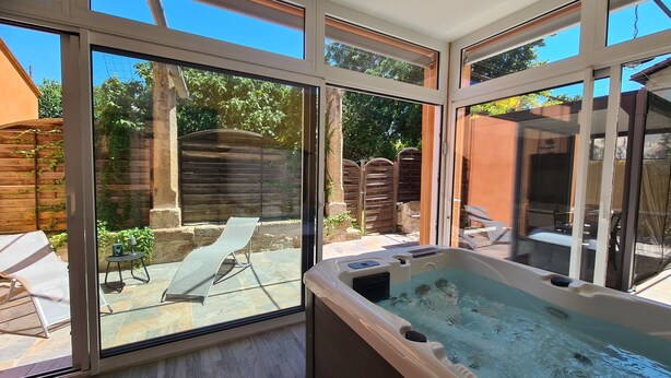 A spa area with a hot tub, a glass door leading to a patio with outdoor furniture, and a view of a garden. - Gîte Le Suquet in the heart of Lambesc near the Pont Royal golf course (Lambesc)