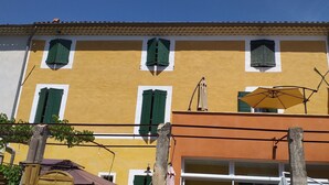 A yellow building with green shutters and a visible garage door. - Gîte Le Suquet in the heart of Lambesc near the Pont Royal golf course (Lambesc)