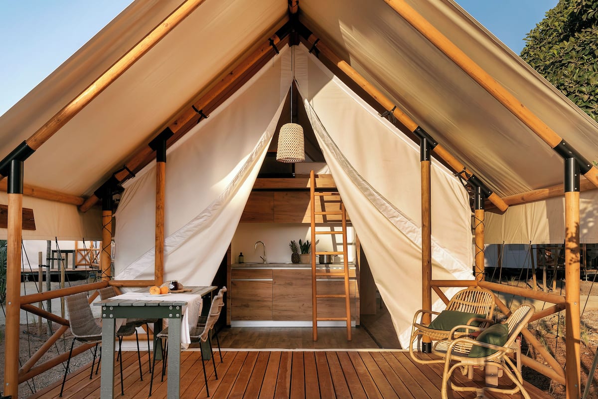 A tent with a wooden deck, a table, chairs, a ladder, and a hanging light fixture.