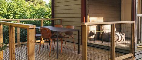 Eine Holzterrasse mit Tisch und Stühlen, ein überdachter Sitzbereich und Blick auf Bäume.