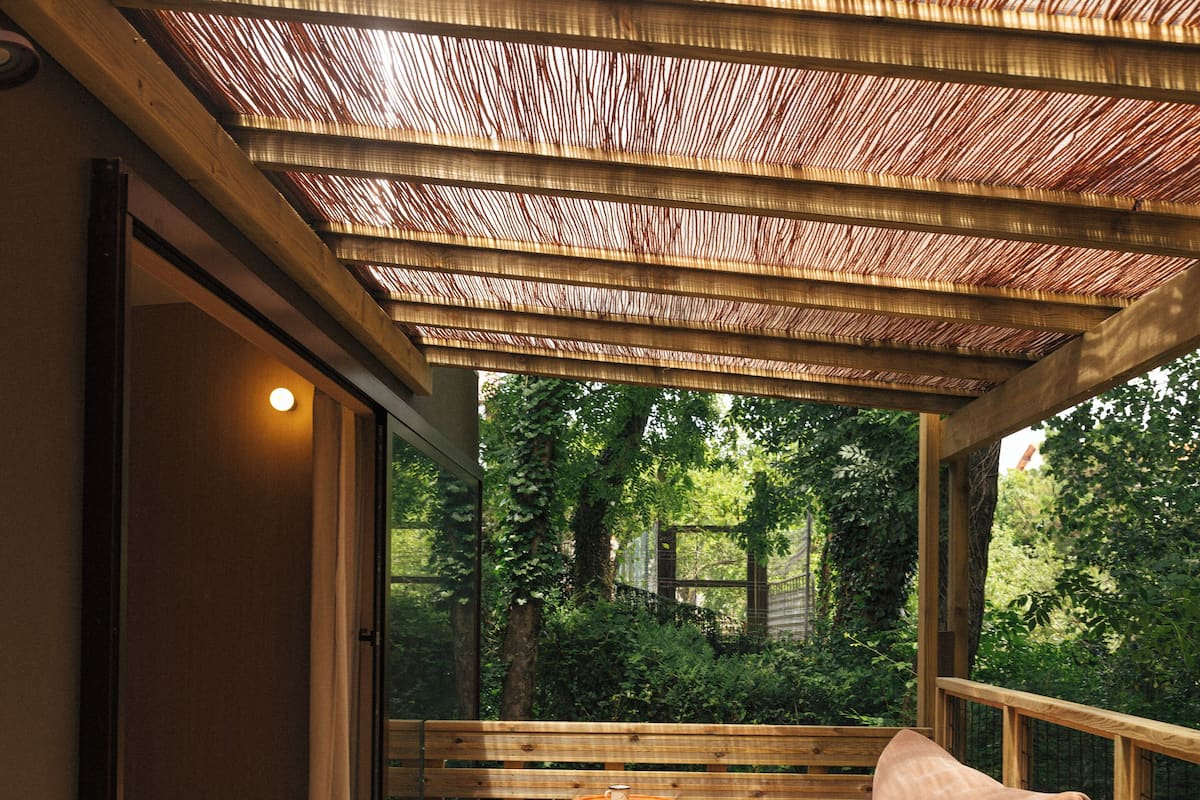 A wooden deck with a bench and a table, overlooking a garden.