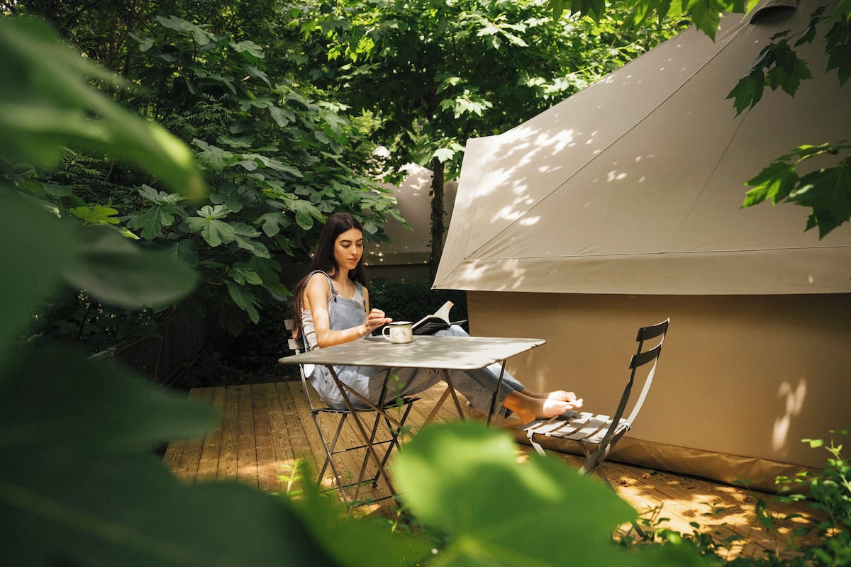 A person sitting at an outdoor table with a tent in the background.
