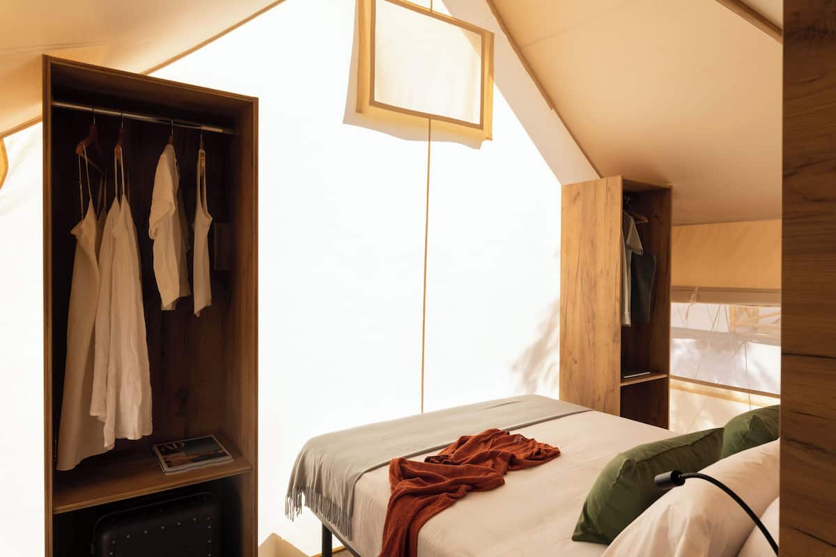 A bedroom with a bed, a wooden wardrobe, and a hanging light fixture.