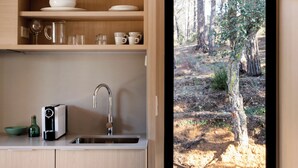 A modern kitchen with wooden cabinets, a sink, and a view of a forest through a glass door. - Wecamp San Sebastian (San Sebastián)