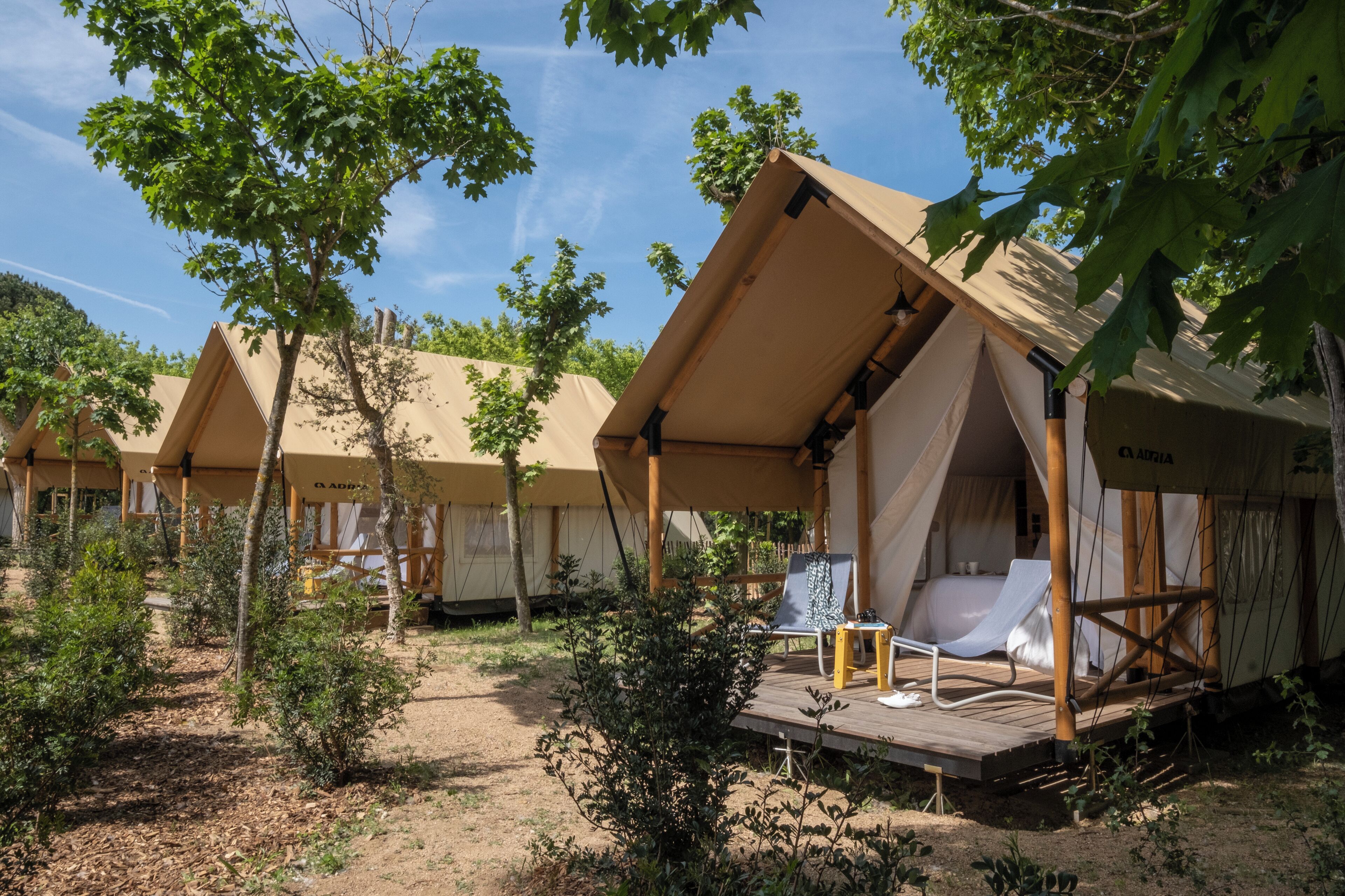 A series of AADRIA tents with a wooden deck, a white chair, and a small table.