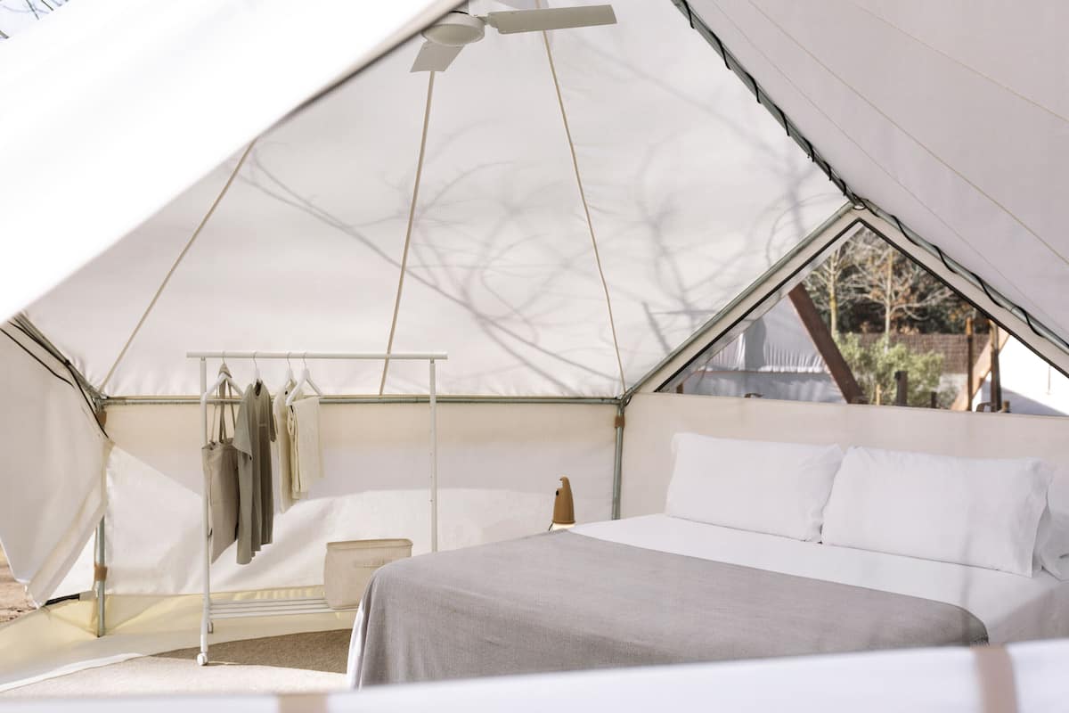 A tented accommodation with a bed, hanging clothes rack, and a small table.
