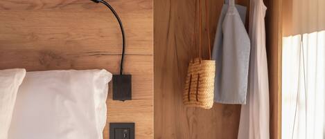 Un dormitorio de madera con cama, mesita de noche y armario empotrado con ropa y zapatos colgados.
