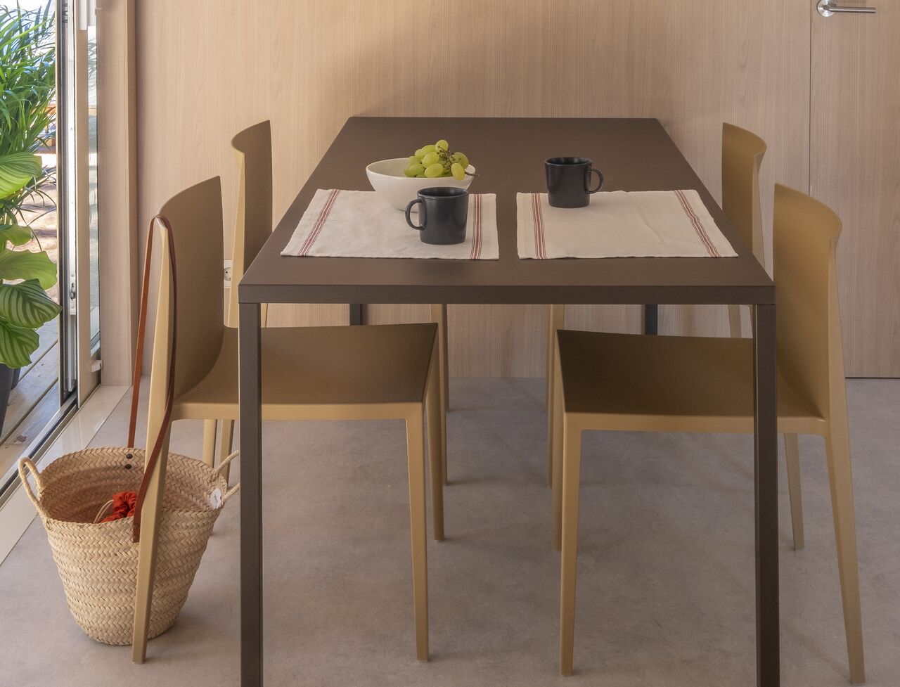 A dining table with four chairs, a bowl of grapes, and two black mugs on placemats.