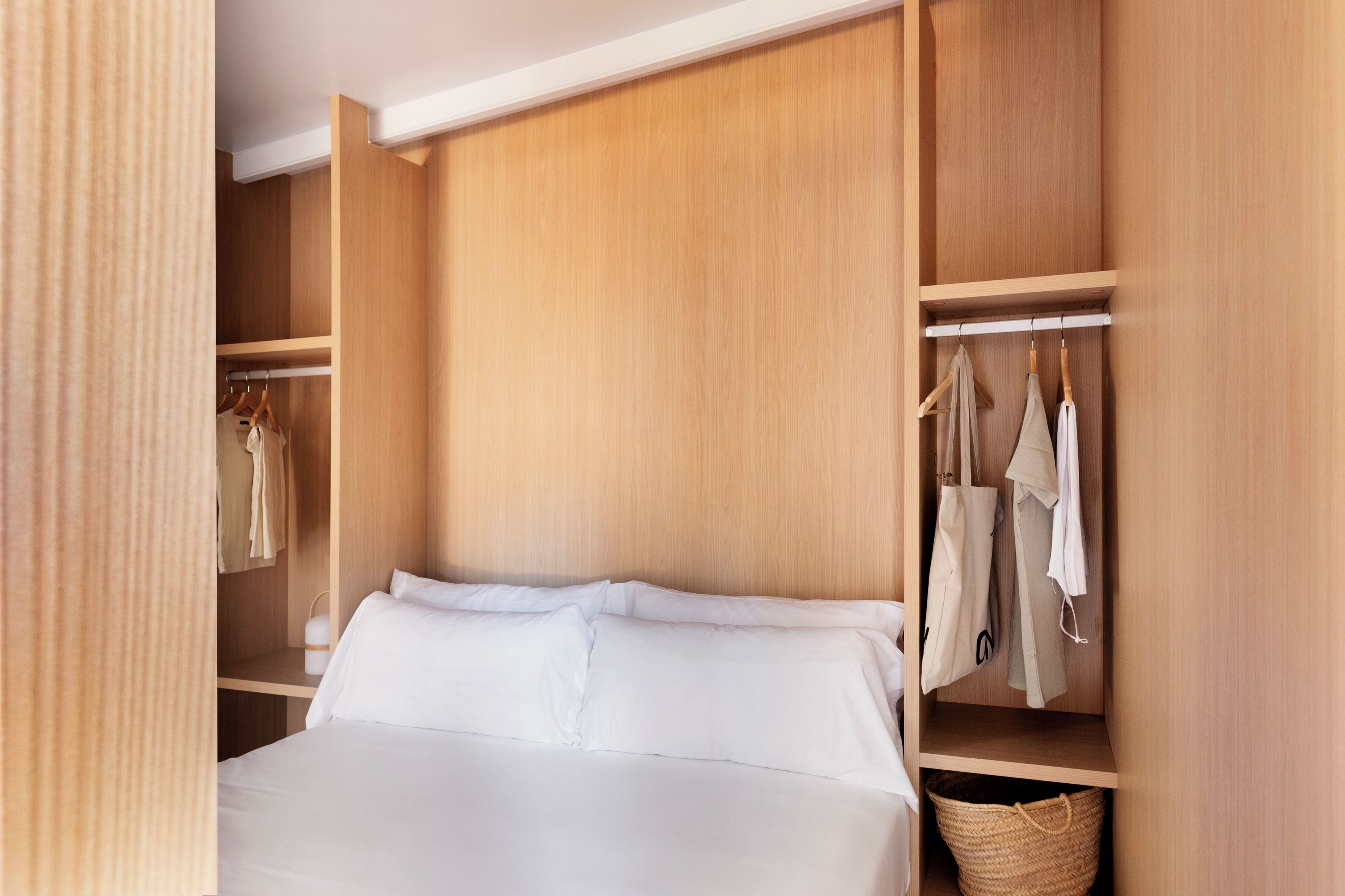 A bedroom with a bed, a wardrobe, and a hanging rack with clothes and bags.