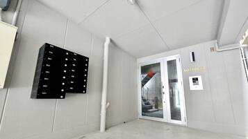 A hallway with a black panel displaying room numbers, a white door labeled "KOTOBUKI," and a small sign with a QR code.