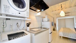 A compact hotel room with a washing machine, a small kitchenette, a bed, and a window with curtains. - Allstay Kotobuki (Naha)