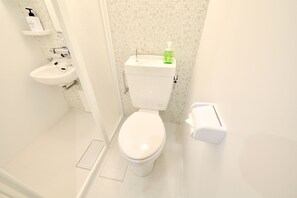 A small, clean bathroom with a toilet, sink, and a soap dispenser on the wall. - Allstay Kotobuki (Naha)