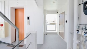 A modern hallway with a staircase, an orange door, and a view of the city through a large window. - Allstay Kotobuki (Naha)