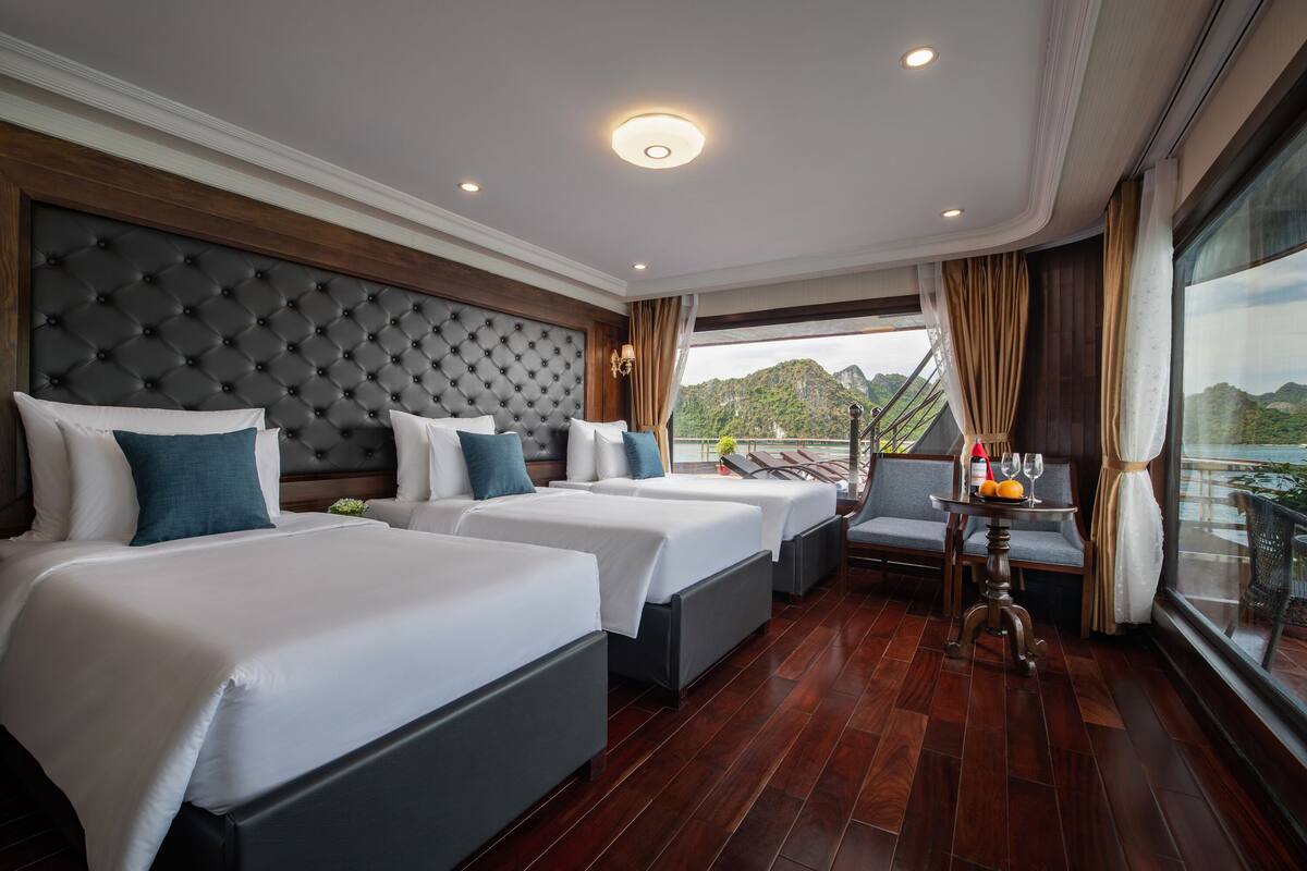A hotel room with two beds, a balcony with a table and chairs, and a view of the mountains.