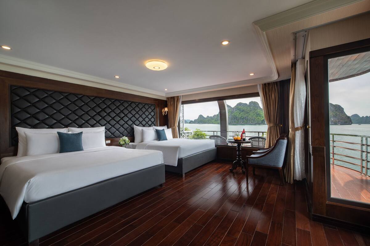 A hotel room with two beds, a dining area, and a large window overlooking a body of water.