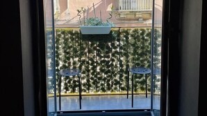 Un balcón con vista a un edificio, dos sillas y una maceta colgante.
