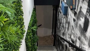 Una escalera con una pared texturizada a la derecha y un muro cubierto de plantas verdes a la izquierda.