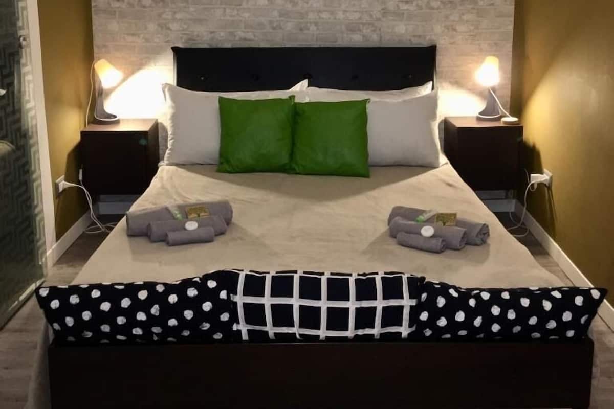 A neatly made bed with a black and white polka dot bedspread, two green pillows, and a black headboard.