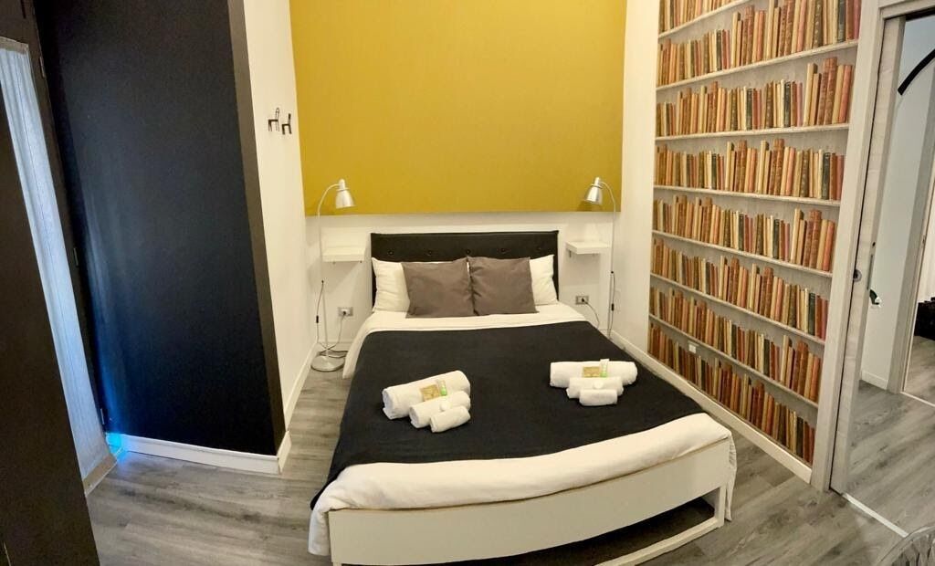 Une chambre à coucher bien rangée, avec un grand lit, des lampes de chevet, une bibliothèque et une porte.