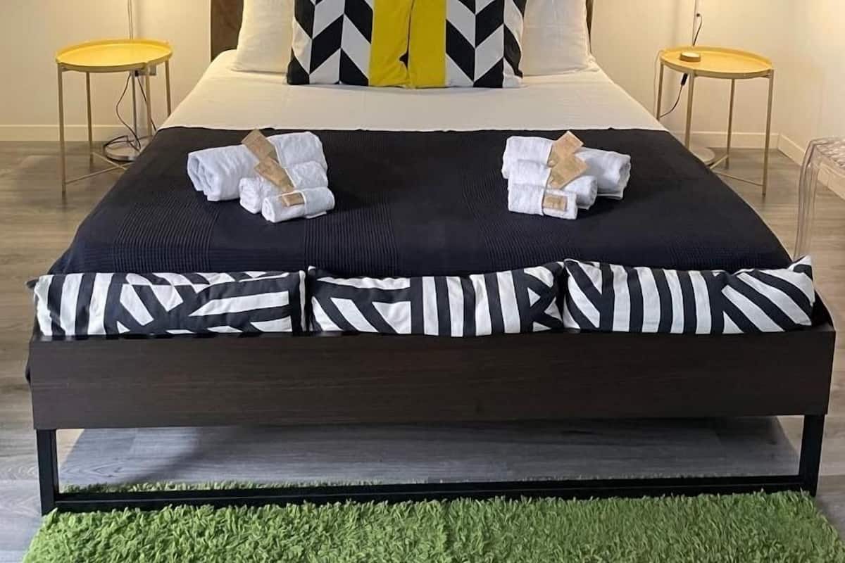 A modern hotel room with a large bed, two bedside tables, and a green rug.