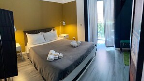 Una habitación de hotel moderna con una cama grande, una mesita de noche, una lámpara y vistas al exterior.