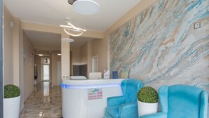 Un área de recepción con suelo de mármol, mostrador de recepción, sillas azules y una pared con diseño de mármol.