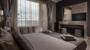 Una habitación de hotel con una cama grande, televisión, escritorio y ventana con cortinas.