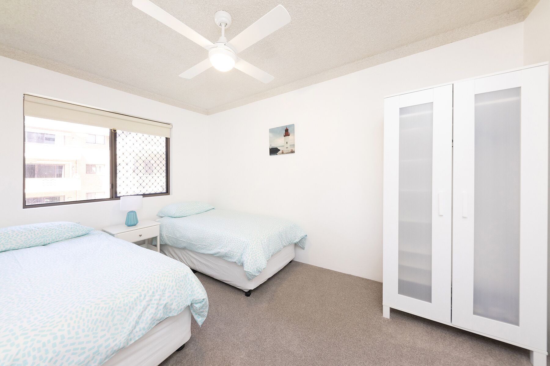 Ein Schlafzimmer mit zwei Betten, einem Deckenventilator, einem Fenster mit Jalousien, einem Bild an der Wand und einem Kleiderschrank.