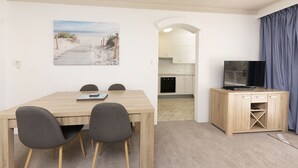 Een ruimtelijk ingerichte leefruimte met een eethoek, kitchenette en een televisie op een houten kast.