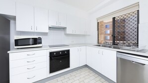 Een moderne keuken met witte kastjes, een magnetron, een vaatwasser en een raam met uitzicht op een bakstenen gebouw.