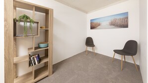 Een kamer met een houten boekenkast, twee stoelen en een schilderij met een strandthema aan de muur.