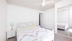 Een slaapkamer met een bed, nachtkastjes, een plafondventilator en een spiegel.