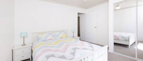 Un dormitorio con cama, mesitas de noche, ventilador de techo y espejo.