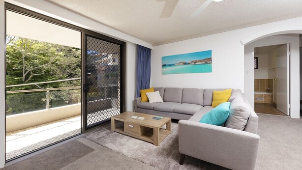 Een moderne woonkamer met een grijze bank, een houten salontafel en uitzicht op een balkon met een stadsgezicht.
