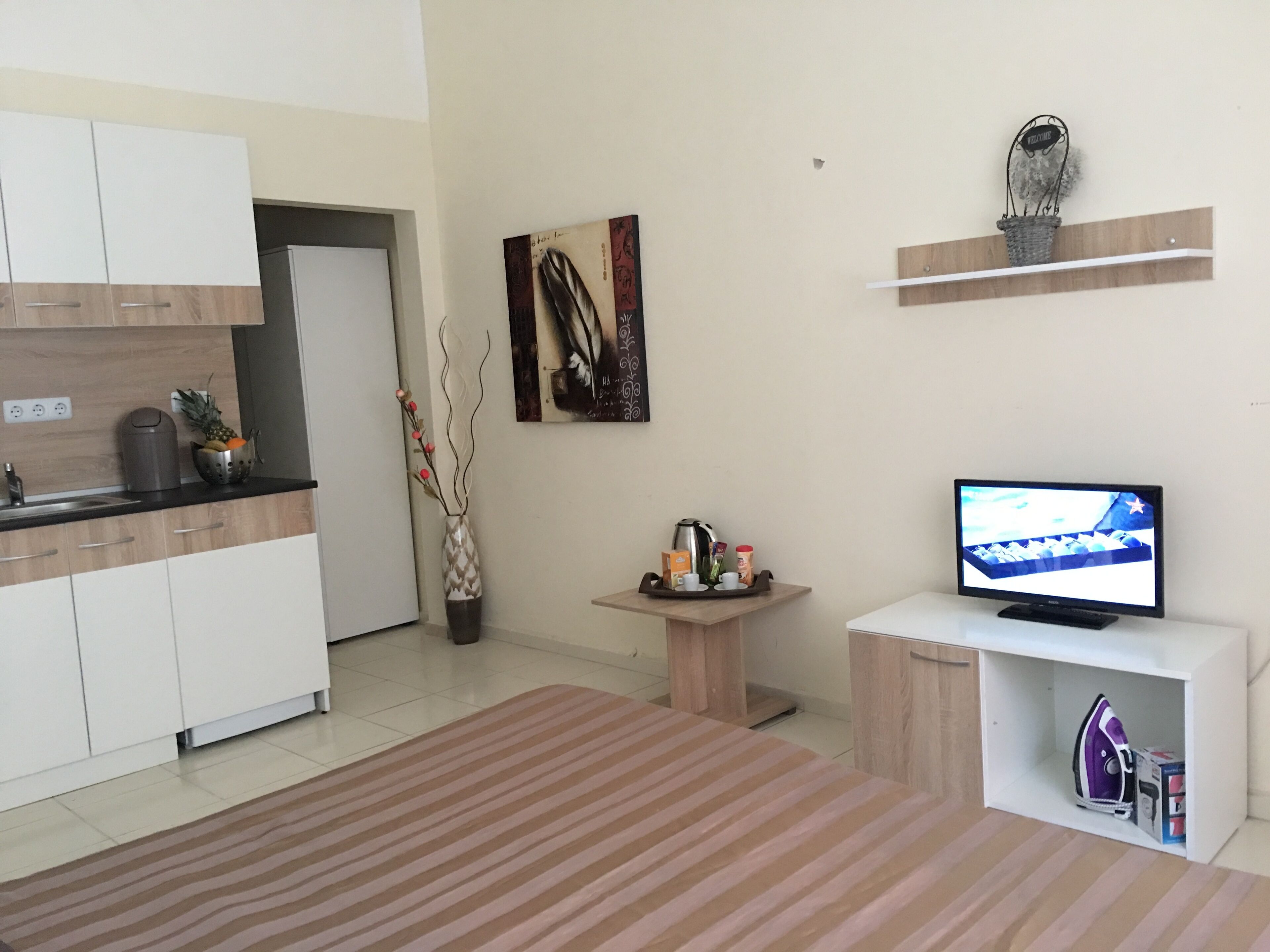 Eine moderne Küche mit weißen Schränken, einer Kaffeemaschine und einer Obstschale. Ein kleiner Tisch bietet Frühstücksgebäck, und an der Wand hängt ein Bild.