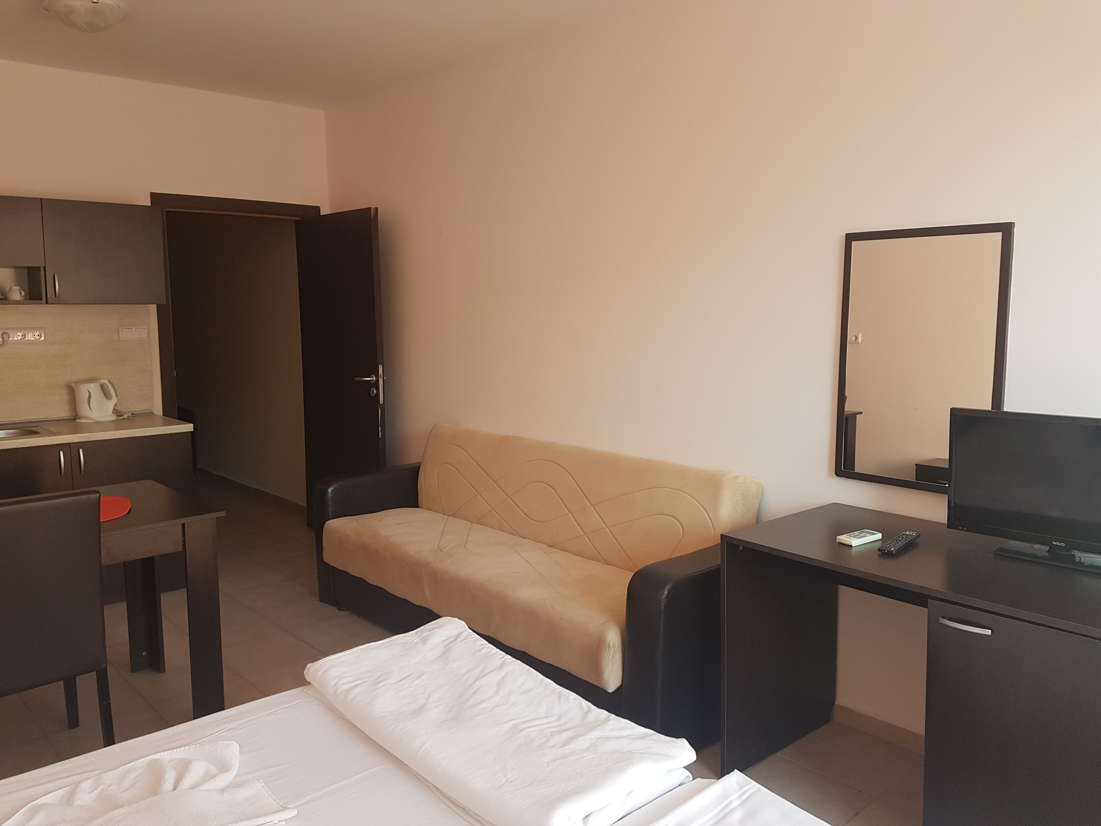 Una camera d'albergo con un letto, una scrivania con un computer, una sedia, un divano, un armadio e uno specchio.