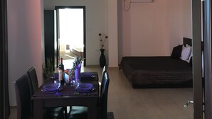 A dining area with a table set for four, a bed in the background, and a door leading to another room. - Sea Breeze Pomorie (Pomorie)