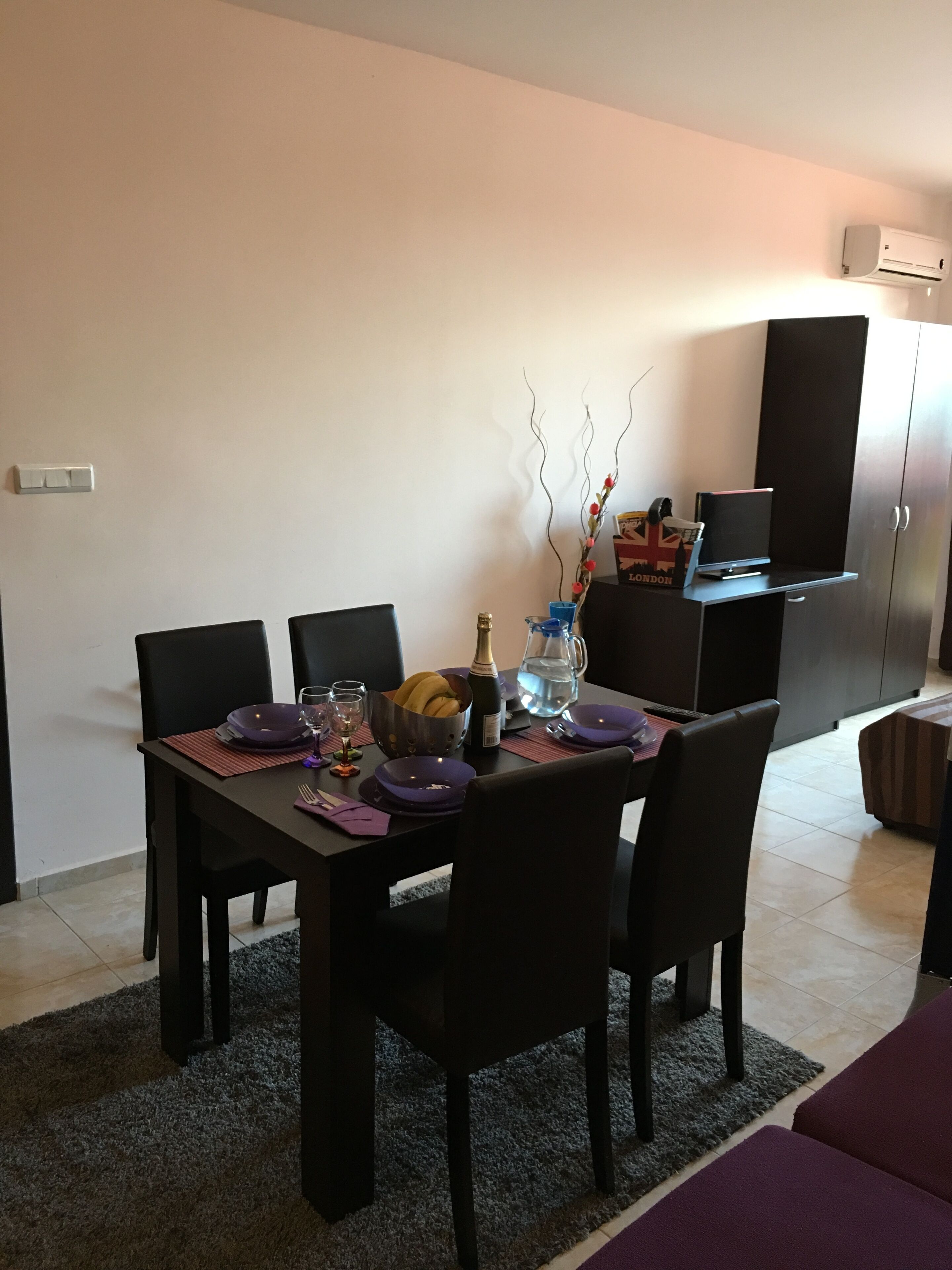 A dining area with a table set for four, chairs, a vase with branches, and a box of London cigarettes.