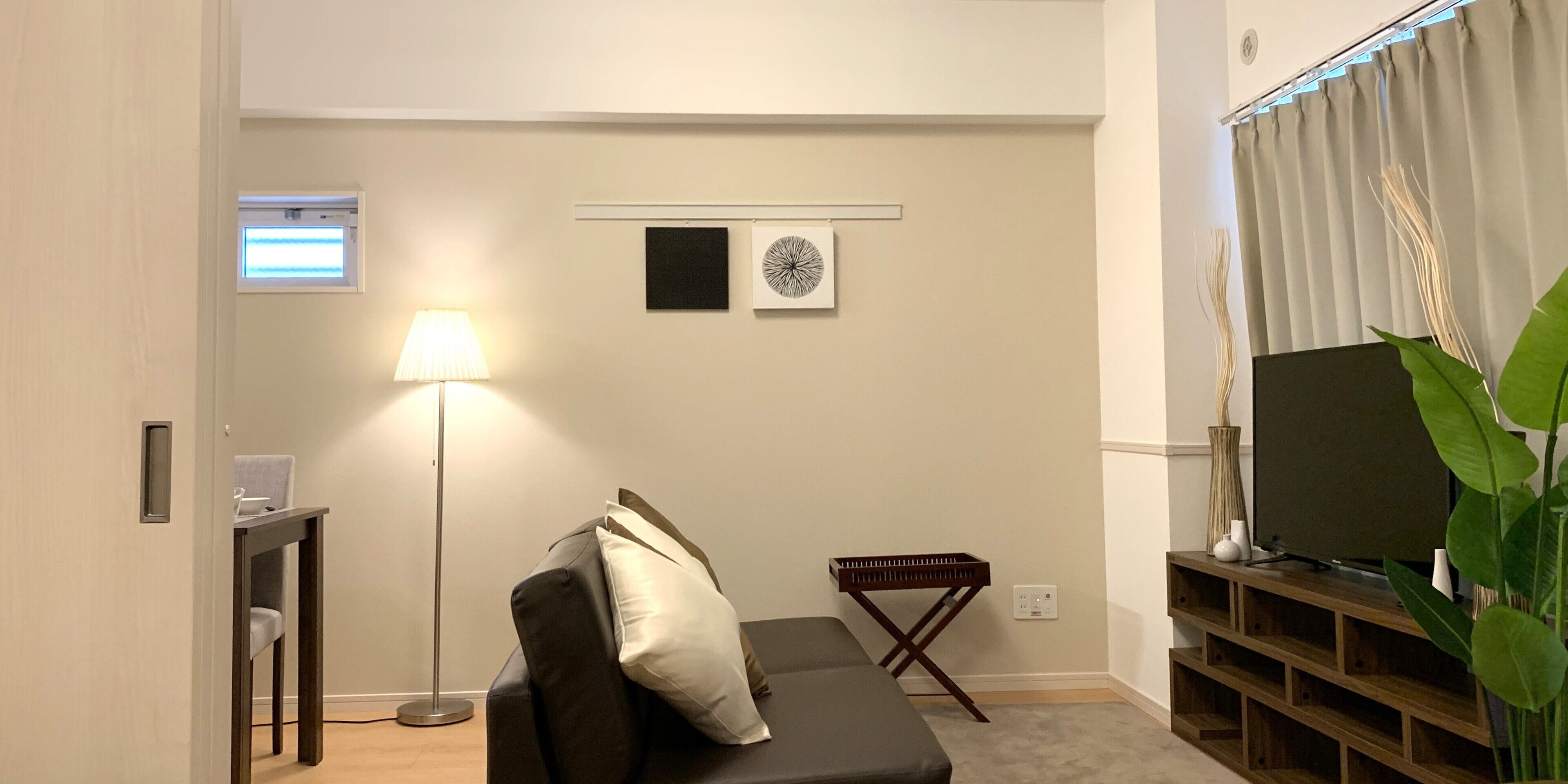 Un salon avec un canapé, un lampadaire, une petite table, un téléviseur et une plante.