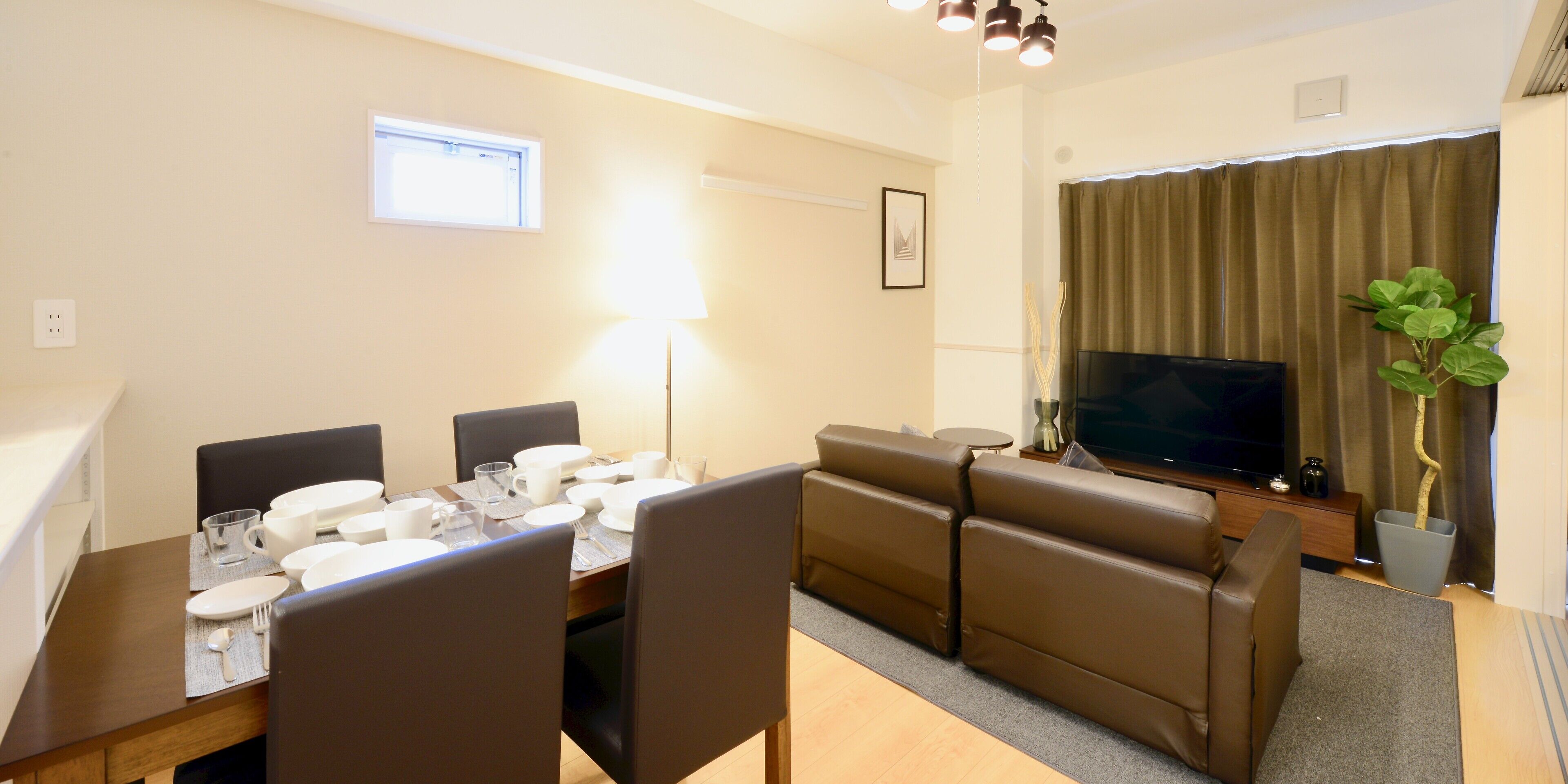 Un comedor con una mesa para cuatro personas, un sofá, un televisor y una ventana con cortinas.