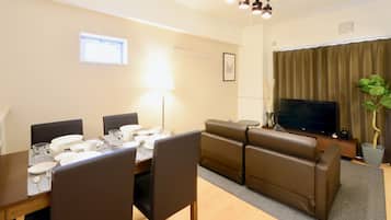 A dining area with a table set for four, a sofa, a television, and a window with curtains.