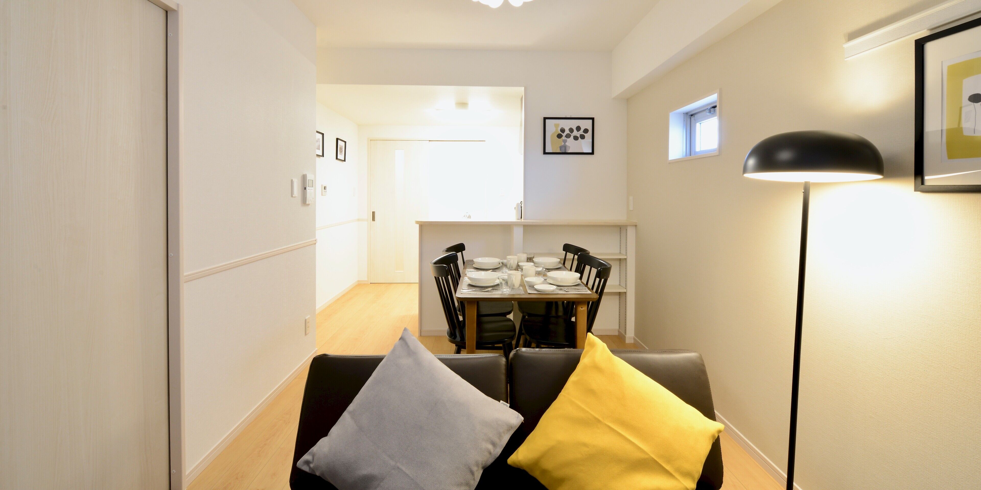 A modern dining area with a table set for four, a black and yellow sofa, and a floor lamp.