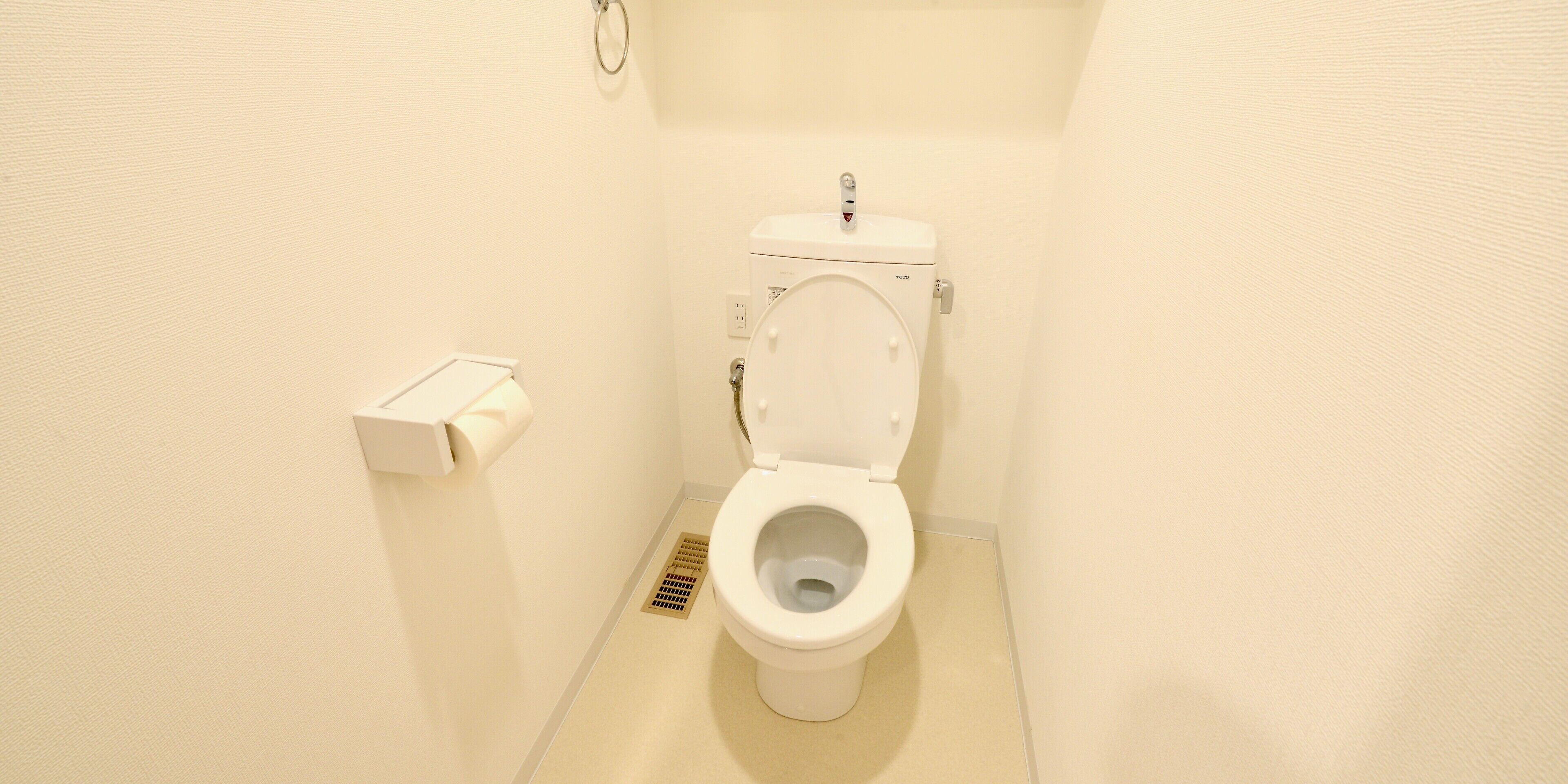 A small, clean bathroom with a toilet, a toilet paper holder, and a floor drain.